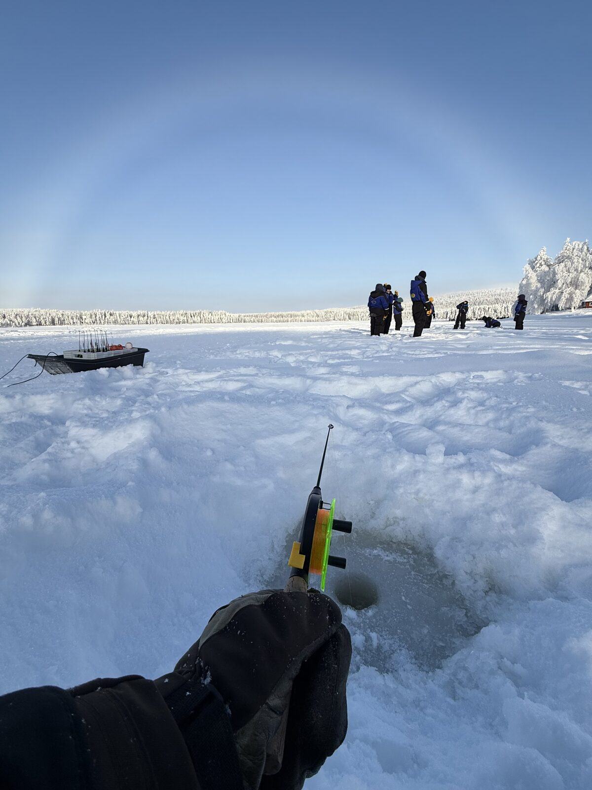 Eisangel durch ein Loch im gefrorenen See, Gruppe im Hintergrund